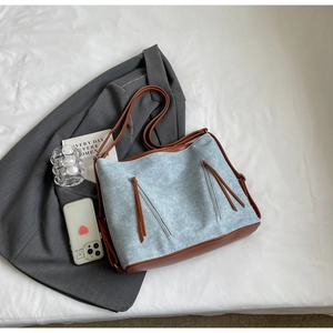 Detail of light blue denim tote with brown leather trim and tassel zippers on white cloth