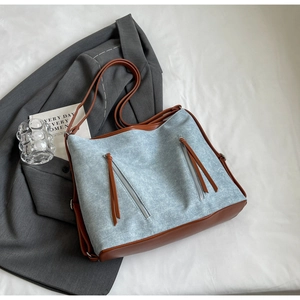Detail of blue canvas tote bag with brown leather trim and dual decorative zippers