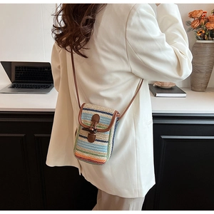 Detail of colorful woven straw crossbody bag with brown leather strap and horn toggle closure