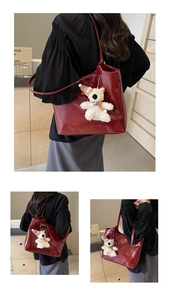 Detail of burgundy tote bag with cute teddy bear charm accessory in cozy indoor setting