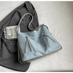 Detailed close-up of light blue textured tote bag with diagonal zipper pockets and silver base