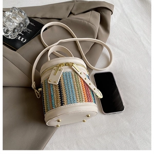 Detail view of woven bucket bag featuring color-block stripes and gold metal feet studs