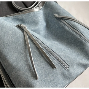 Close-up of light blue denim tote bag with silver dual zippers and textured fabric