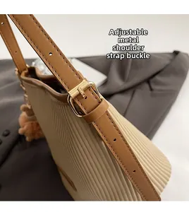 Detail of adjustable leather strap with gold hardware on pleated cream bucket bag