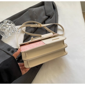 Dettaglio di una borsa a tracolla beige e rosa su un blazer grigio con accessori