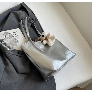 Close-up of metallic silver tote bag with white plush bear on dark grey suit