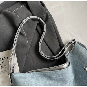 Detail of light blue denim tote with silver metallic straps and vintage wash texture
