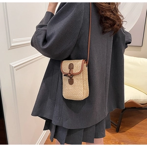 Detail of a straw crossbody phone bag featuring a brown leather trim and horn buckle closure