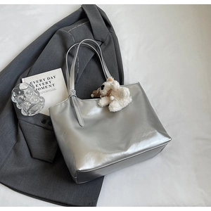 Flat lay of a silver glossy tote bag with a white plush bear charm and fashion props