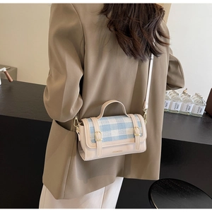 Detail view of contrast color crossbody bag with blue plaid flap and gold buckle on model