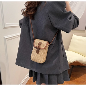 Detailed shot of a woven straw phone bag with brown leather trim and horn buckle