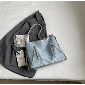 Detail of light blue denim tote bag with long tassel zippers and silver-grey stitching