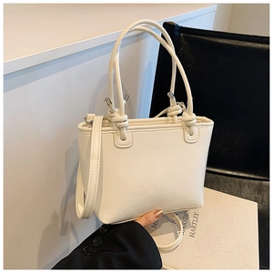 Detail of minimalist cream bucket bag with unique knot handle and smooth leather texture
