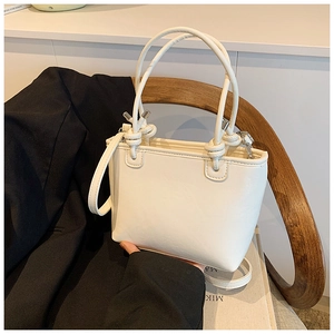 Detail showing the white bucket bag with elegant knot handle and detachable strap
