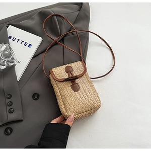 Detail of woven straw phone bag with brown leather trim and horn buckle closure