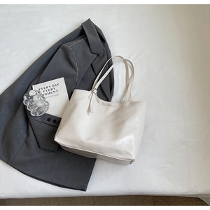 Minimalist beige glossy tote bag styled on white linen with a gray blazer