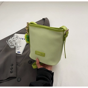 Detail of green corduroy bucket bag texture with gold hardware and plush charm on suit