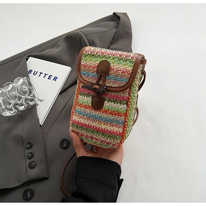 Detail of colorful woven straw bag featuring a brown faux leather flap and horn buckle