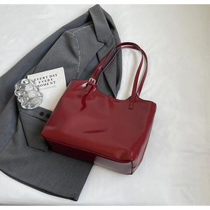 Macro detail of glossy wine red patent leather tote bag with silver metal buckles
