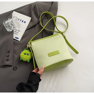 Detail of light green corduroy bucket bag with plush monster charm and leather accents