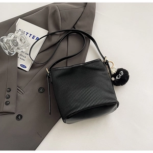 Close-up of black pleated bucket bag with a cute plush eye charm on a gray blazer