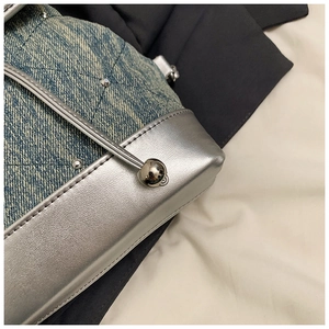 Détail d'un sac à dos en jean matelassé bleu clair avec clous argentés et garniture cuir