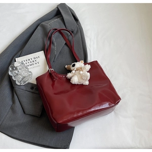 Detail of burgundy PU leather tote bag with a white knit bear charm on dark blazer