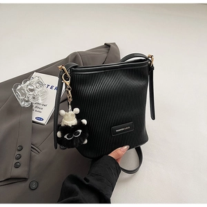 Detail of black pleated bucket bag with vertical texture and cute plush charm accessory