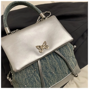 Détail du rabat argenté avec boucle papillon sur un sac à dos en denim matelassé