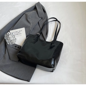 Detail of glossy black patent leather tote bag with metallic buckle on white fabric
