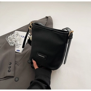 Detailed view of the black bucket bag's vertical pleated texture and golden metal buckle