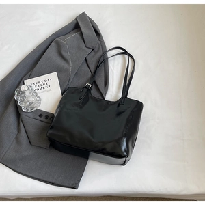 Detailed shot of black patent leather tote bag with silver buckle and glossy texture