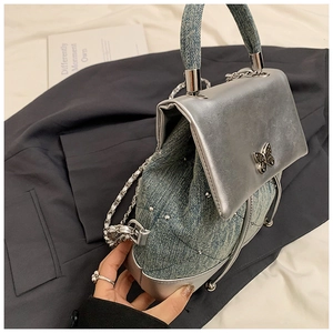 Détail du sac en denim bleu et cuir métallisé argenté avec ornement papillon en métal
