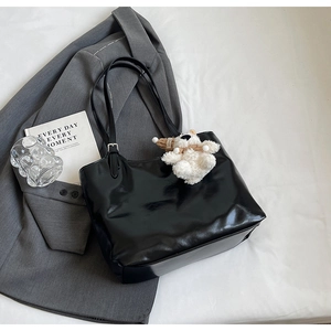 Detail of black patent leather tote bag with plush bear charm and silver buckle