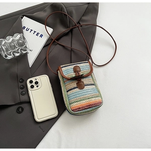 Close-up of rainbow striped straw woven phone bag with brown leather flap and horn buckle