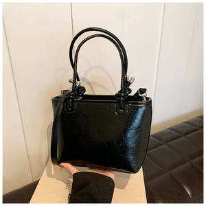 Close-up of black glossy bucket bag with pleated texture and silver hardware details