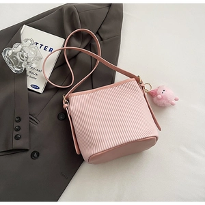 Detail of pink pleated bucket bag with plush charm on a textured grey blazer background