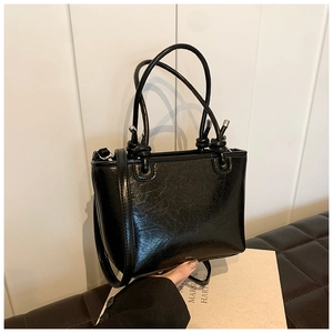 Detail view of black glossy bucket bag featuring dual knotted handles and silver hardware