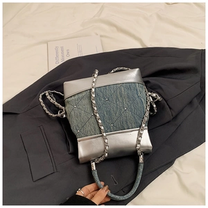 Détail du sac seau en jean bleu avec clous argentés et chaîne sur un blazer gris