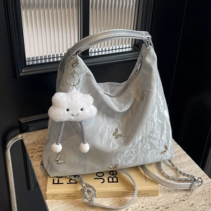 Grande borsa tote argento con ciondolo a farfalla e nuvola di peluche su scrivania