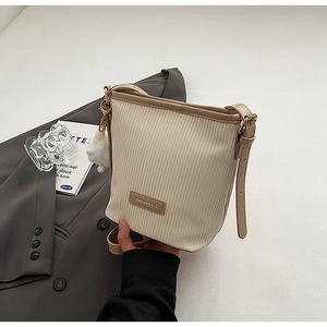 Detail of pleated bucket bag with brown leather trim and cute pompom accessory