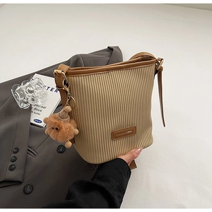 Detail view of corduroy bucket bag featuring leather trim and brown plush pendant