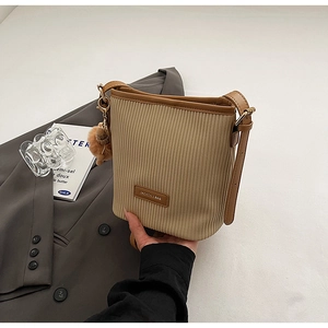 Detail of beige pleated bucket bag featuring brown leather trim and a plush ball charm