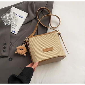 Close-up of pleated beige bucket bag with brown leather trim and plush charm