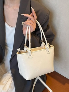 Minimalist cream bucket bag with knot handle and shoulder strap shown on model