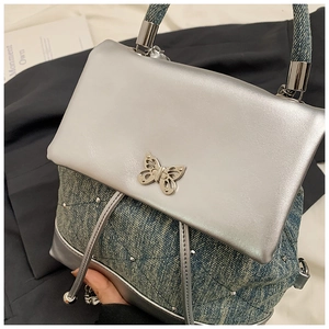 Détail du sac argenté en denim avec ornement de papillon métallique et perles