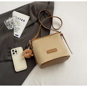 Detail of beige corduroy bucket bag with leather strap and plush pompom charm