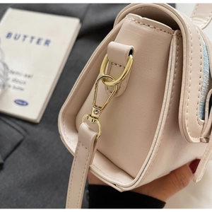 Detailed close-up of golden hardware and stitching on a minimalist cream crossbody bag