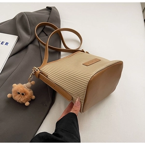 Close-up of pleated beige bucket bag with brown leather trim and cute bear charm decoration