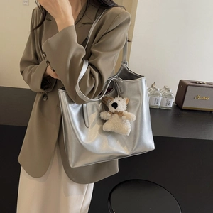 Minimalist silver faux leather tote bag with plush bear charm worn by a model